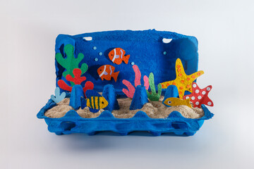 Handmade underwater diorama in blue egg carton with paper fish, corals, sand. DIY ocean craft for kids, creative recycling project. Useful for eco-friendly brands, craft workshops, educational