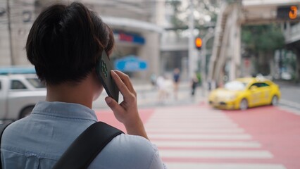 Businessman talking on smartphone while standing on city street with taxi cab and crosswalk in...