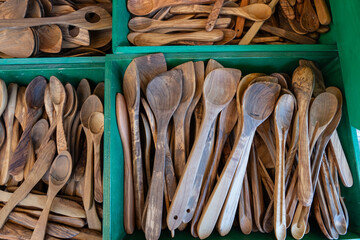 A collection of handcrafted wooden kitchen utensils, primarily spoons, displayed in green boxes,...