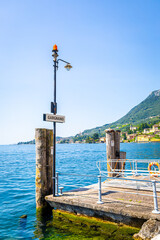Streetlamp and Gargnano signpost by Lake Garda, Italy, with clear blue sky and calm lake waters, ideal for travel and destination visuals