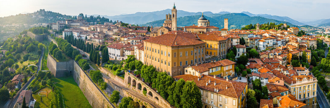 Aerial view of Bergamo&rsquo;s Citt&agrave; Alta in Italy with terracotta rooftops, historic churches, and mountain backdrop on a clear day