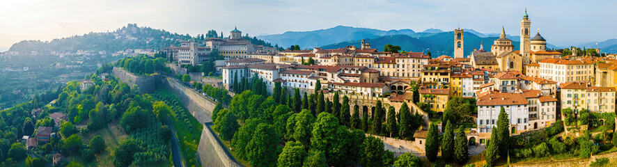 Obraz premium Aerial view of Bergamo’s Città Alta in Italy with terracotta rooftops, historic churches, and mountain backdrop on a clear day
