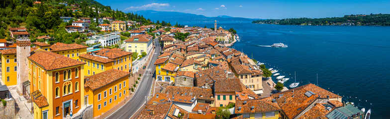 Aerial view of Salo, Italy with terracotta rooftops, lakeside promenade, and boats docked on the shore of Lake Garda on a sunny summer day