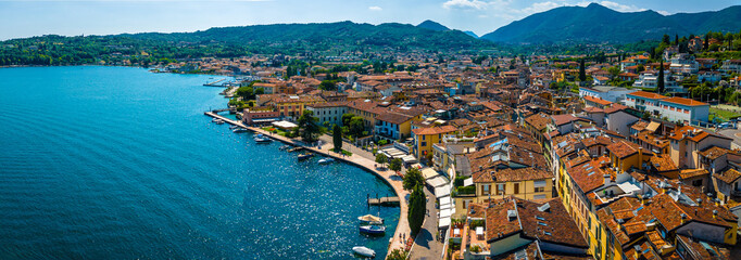 Aerial view of Salo, Italy with terracotta rooftops, lakeside promenade, and boats docked on the shore of Lake Garda on a sunny summer day