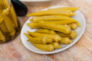 Pickled okra pods on plate on wooden table, homemade preserves