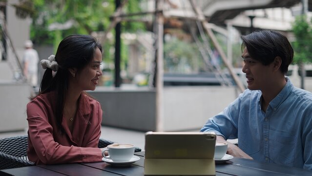 Professionals sharing coffee moment, collaborating over tablet at sunny urban cafe patio, networking casually