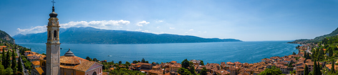Fototapeta premium Aerial view of a pink historic church with bell tower in Gargnano, Lake Garda, Italy, surrounded by mountains and blue lake waters.