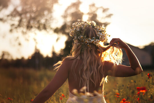 Young blonde woman in a wreath of daisies on a flower field at sunset - Powered by Adobe