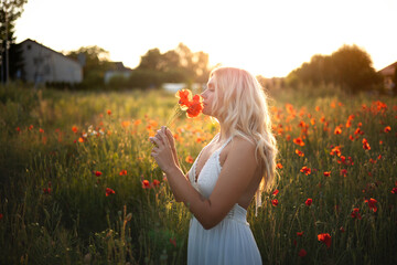 young beautiful blonde woman in white dress in poppy field at sunset. Woman and nature