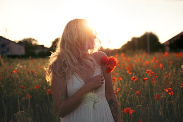 young beautiful blonde woman in white dress in poppy field at sunset. Woman and nature