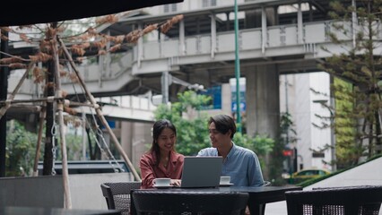 Businesspeople collaborating over laptop, sipping coffee at bustling bangkok outdoor cafe