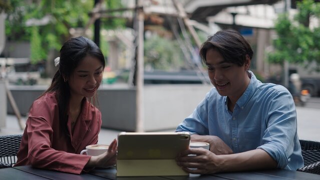 Two young professionals are using a tablet and drinking coffee at an outdoor cafe