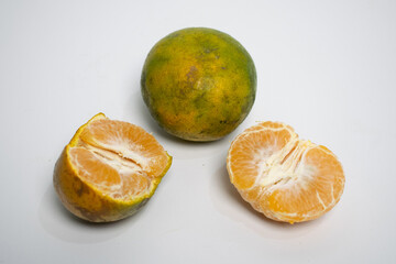 A fresh orange with greenish skin, shown whole and cut open to reveal its juicy segments.