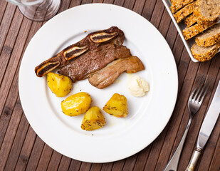 Succulent grilled steak with slices of potato served in a plate with other table appointments