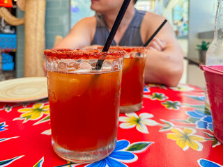 Michelada cocktail sitting on red floral tablecloth with restaurant patron waiting