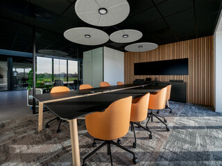 Modern conference room with orange chairs, black table, wood accent wall, and circular ceiling lights