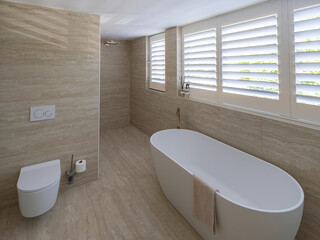 Luxury marble bathroom with freestanding bathtub, wall-mounted toilet, glass shower, and brass...