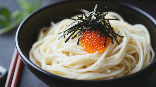 A bowl of japanese udon noodles topped with seaweed and salmon roe is presented