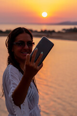 Happy woman taking selfie through smart phone at beach at sunset. Romantic night at seaside.