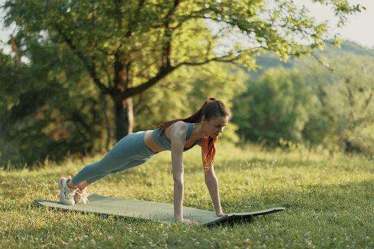 Young woman practicing outdoor fitness in serene green nature, wearing sports attire, showing determination and focus while performing a plank exercise