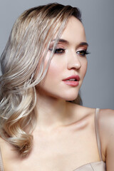 Portrait of young blonde woman. Female in beige dress on straps on gray background