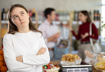 Tired and brassed off girl stands in store and waits for resolution of quarrel between parents....