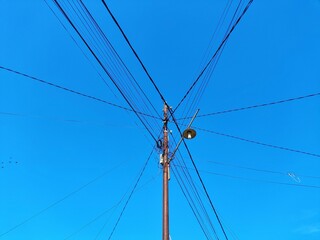 Electric pole with tangled cables and street lights, with a clean and bright blue sky background