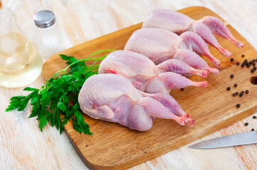 Four uncooked quails on wooden board with parsley black pepper. Preparing food concept.