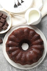 Tasty bundt cake, pieces of chocolate and milk on grey table, flat lay