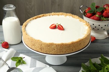 One tasty cheesecake, strawberries, mint and milk on grey table against wooden background, closeup