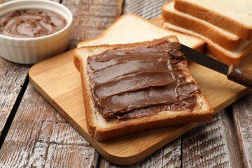 Sandwiches with chocolate butter and knife on wooden table, closeup