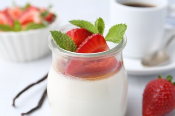 Tasty panna cotta with caramel, strawberries, mint, vanilla pods and coffee on white table, closeup