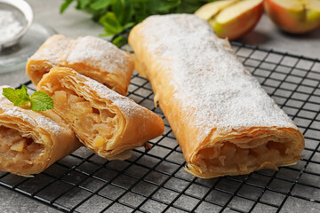 Tasty apple strudels with powdered sugar and mint on grey table, closeup