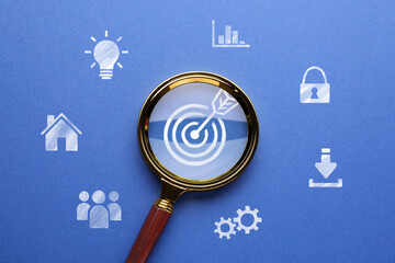 Magnifying glass over target with arrow on blue background, top view. Different icons around