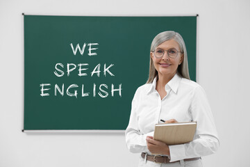 Teacher near green chalkboard with text We Speak English. Language course