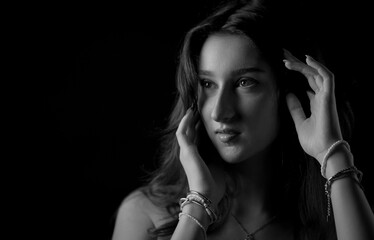 Dramatic black and white portrait of a young woman with long hair, touching her face and looking...