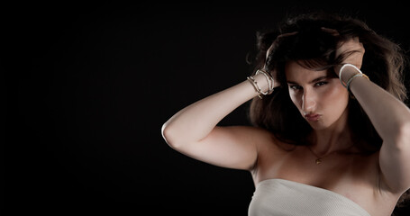 Naklejka premium Studio portrait of a young woman holding her hair with bracelets and a necklace on black background
