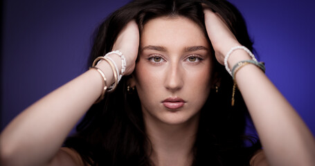 Studio portrait of a young woman holding her long brown hair with her hands wearing bracelets on a...