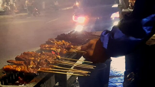 Local Asian Street Food: Chef Cooking Chicken Satay on a Long Stove at Night