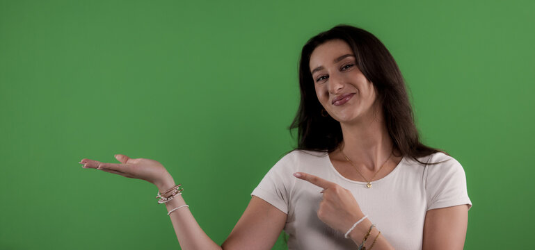 Young woman pointing and showing copy space with hand on green screen background