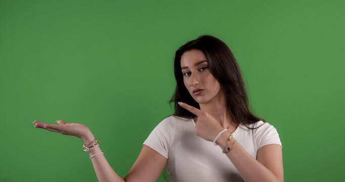 Young woman showing and pointing with index finger at her open hand, isolated on green screen background
