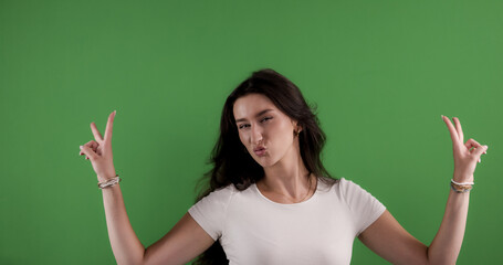 Young woman making a funny face and showing peace sign with both hands on chroma key background
