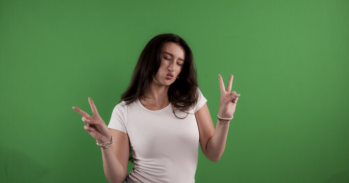 Young woman making a kissy face and showing peace sign with both hands on chroma key background