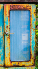 A rusted, turquoise metal cabinet with a rectangular window and a silver handle