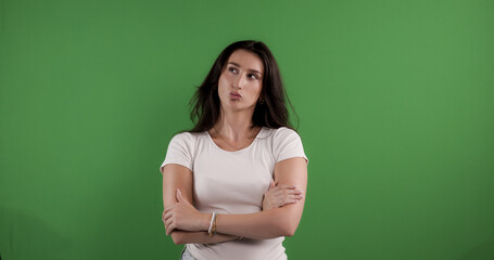 Young woman with crossed arms making a thinking expression on green screen background