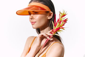Young woman in an orange visor holding colorful tropical flowers, radiating joy and summer vibes.