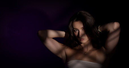 Studio portrait of a young woman with arms raised, casting striped shadows on her face and body...