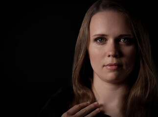 Studio portrait of a young woman with long brown hair and green eyes, wearing a dark dress, with...