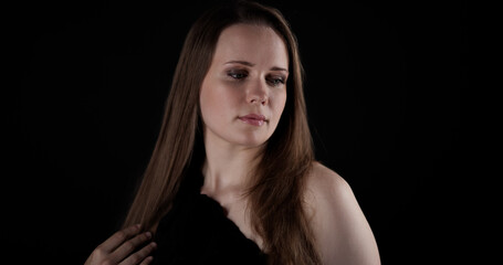 Fototapeta premium Pensive young woman with long brown hair looking away on black background
