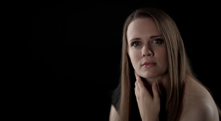 Fototapeta premium Studio portrait of a young Caucasian woman with long light brown hair, touching her neck with her hand